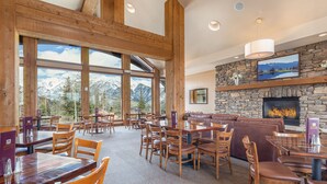 A spacious dining area with wooden tables and chairs, a stone fireplace, and large windows offering mountain views.