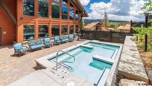 A pool area with two pools, lounge chairs, and a building with large windows.