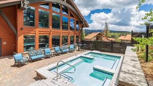 A pool area with two pools, lounge chairs, and a building with large windows.