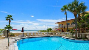 Una piscina con vistas a la playa, palmeras y un edificio con balcones.