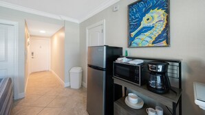 Una cocina compacta con refrigerador, microondas, cafetera y un cuadro en la pared.