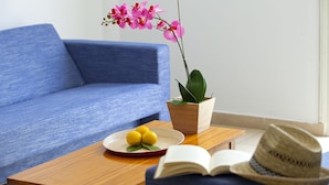 A modern living room with a blue sofa, a wooden coffee table with a plate of lemons and a book, and a potted orchid.