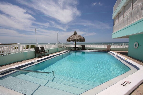 A clear blue pool with a thatched umbrella, white fence, and lounge chairs.