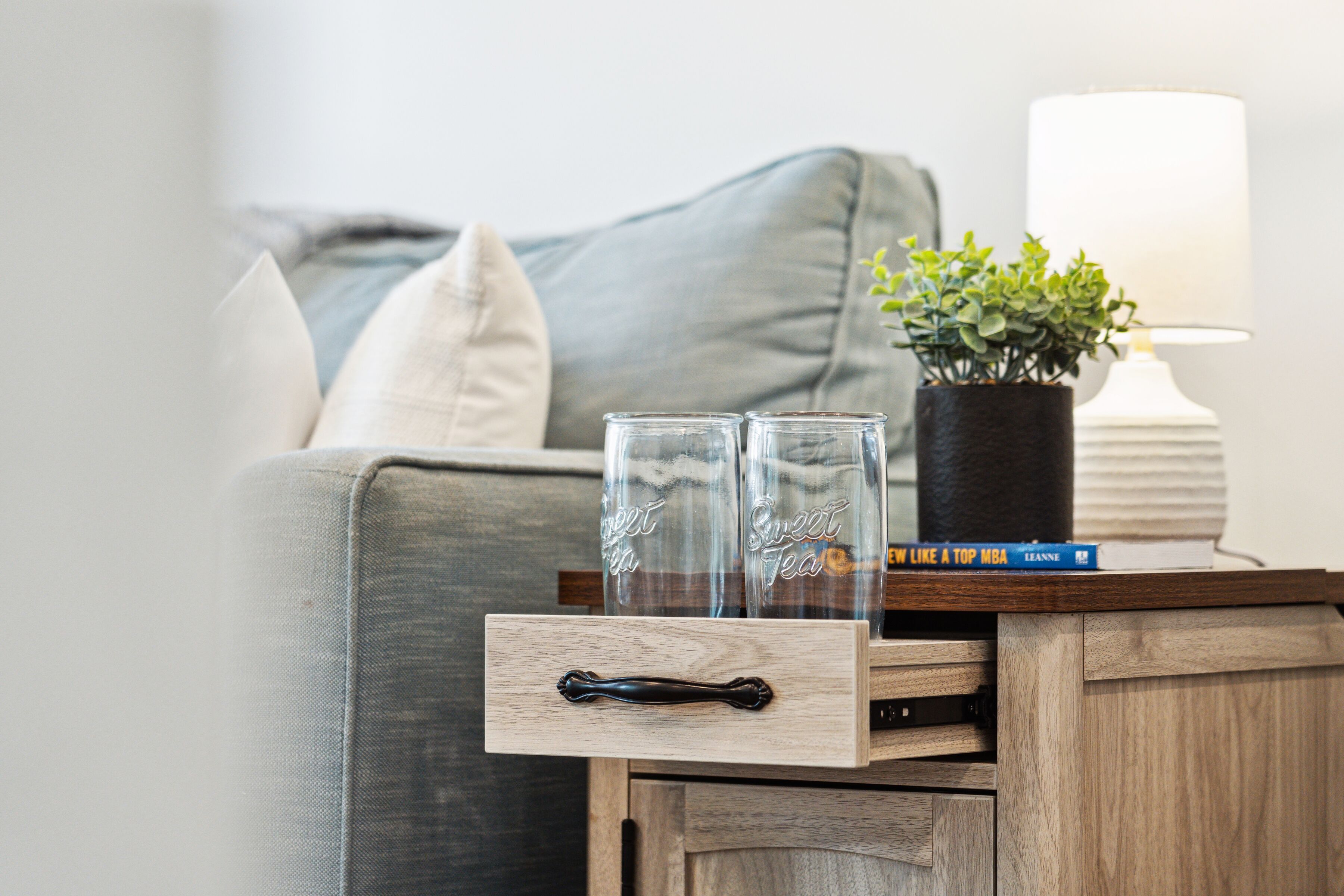Une petite table d’appoint en bois, sur laquelle se trouvent un bocal en verre, un livre intitulé « Comme un étudiant en MBA de premier plan » et une petite plante en pot.