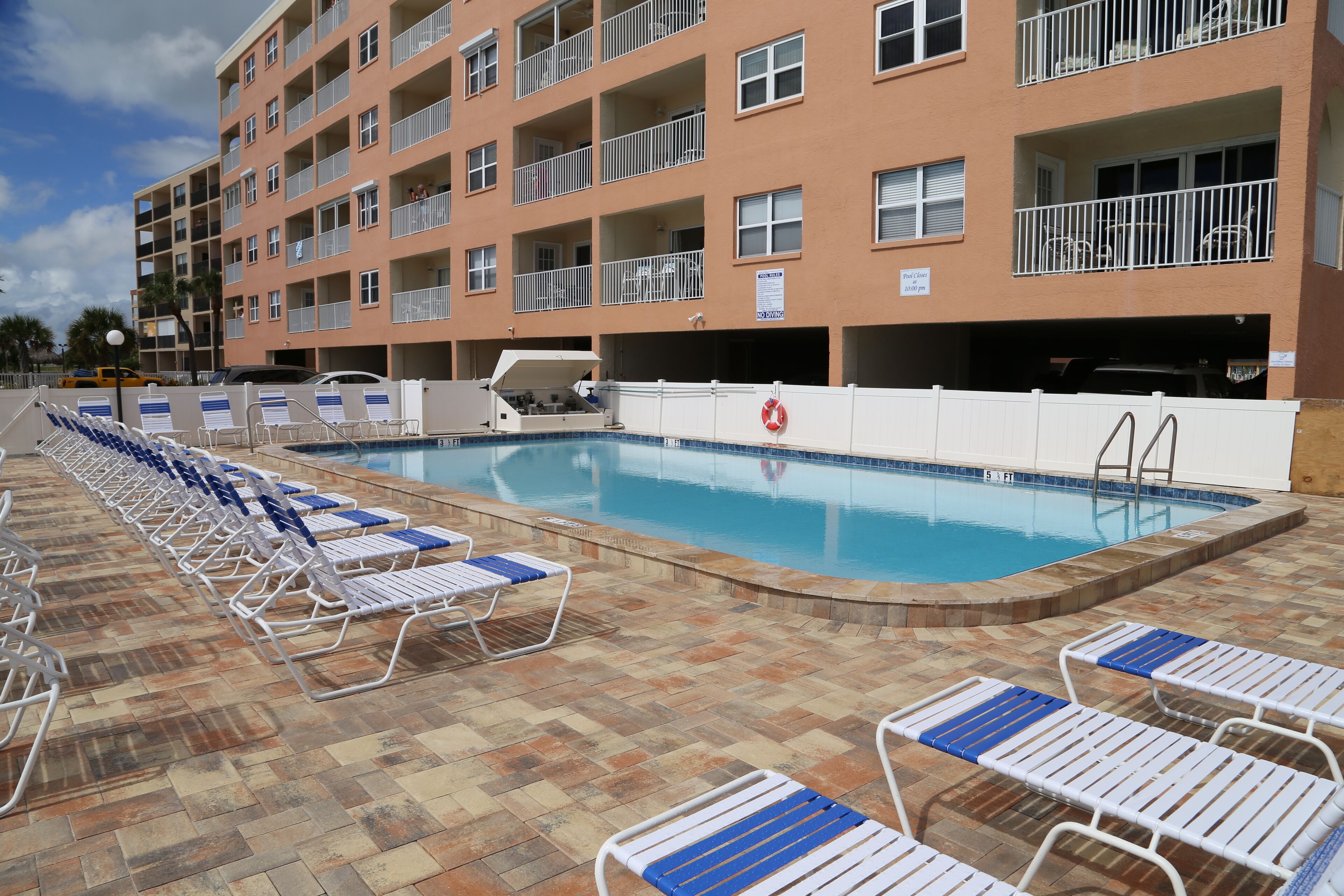 Una piscina con sillones de descanso y un edificio con balcones al fondo.