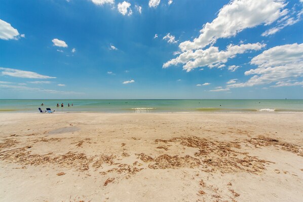 Una extensa playa de arena con cielo azul despejado y nubes dispersas.
