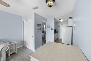 A room with a white door, a small table, a ceiling fan, and a view into the kitchen area. - 1br 1b Beach View - Surf Song #332 (Madeira Beach)
