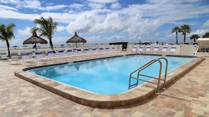 Ein Pool mit gefliestem Deck, Liegestühlen, Palmen und Blick auf den Strand.