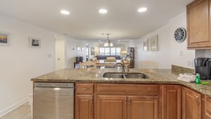 A modern kitchen with granite countertops, wooden cabinets, a stainless steel sink, and a dishwasher. - Beachfront Complex - 2b 2b - Beach Place #503 (Madeira Beach)