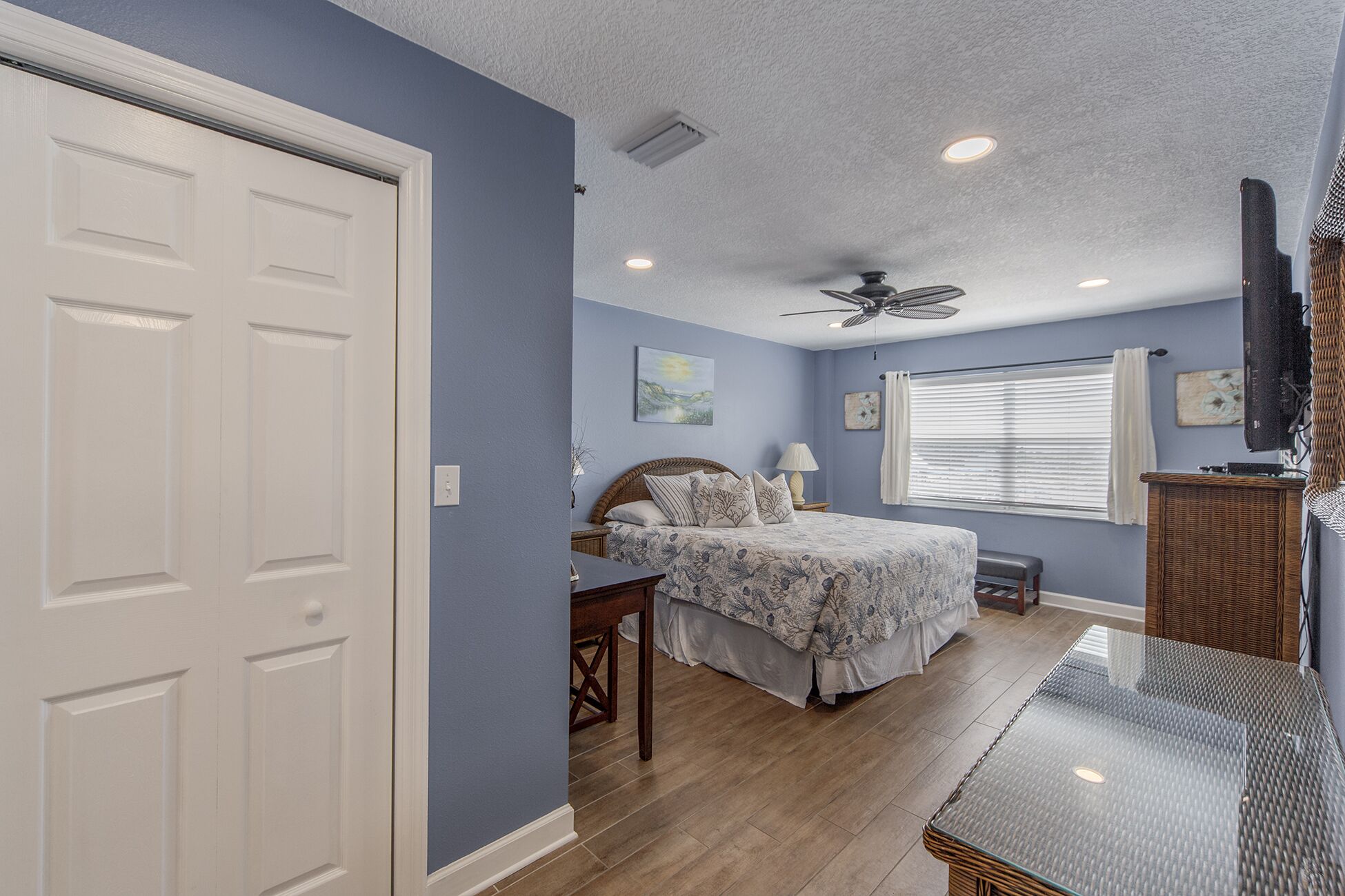 A bedroom with a bed, a desk, a ceiling fan, and a window with blinds.