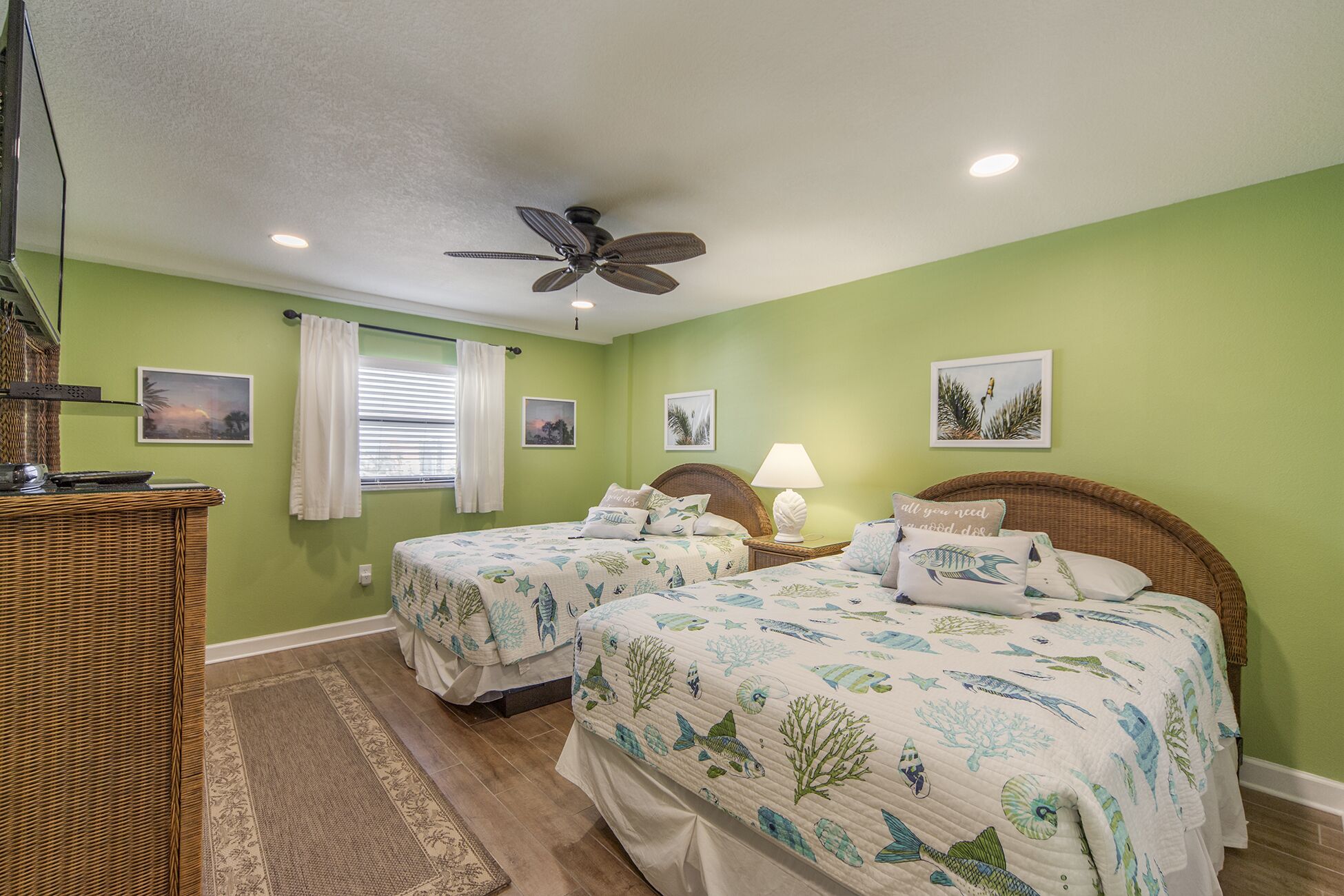 A room with two beds, a ceiling fan, and a window with curtains.