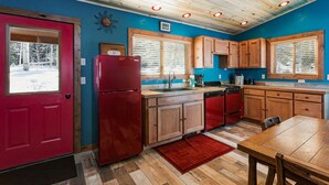 A kitchen with wooden cabinets, a red refrigerator, and a window with blinds.