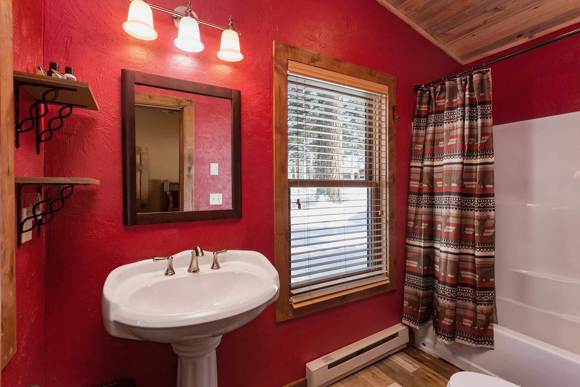 A bathroom with a white sink, a mirror, a window with blinds, a shower curtain, and a red wall.