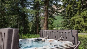 A hot tub in a forested area with tall trees and a clear view of the surrounding landscape.