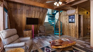 A wooden interior with a leather sofa, a wooden coffee table, a TV, and a spiral staircase.