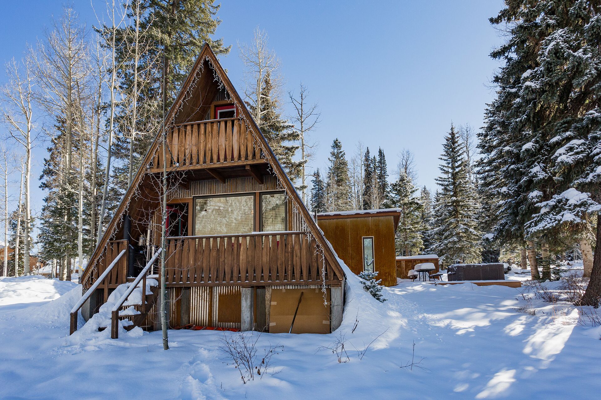 A wooden cabin with a triangular roof, surrounded by snow-covered trees.