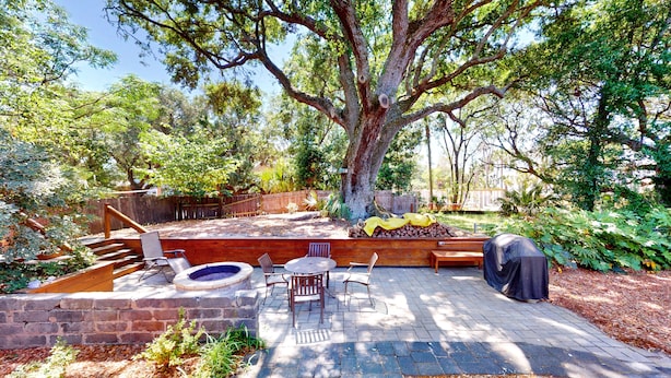A backyard with a fire pit, outdoor seating, and a large tree.