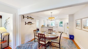 A dining area with a round table, chairs, and a chandelier. There are fish mounted on the wall and a kitchen in the background.