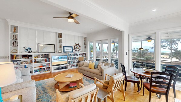 A spacious living room with a large TV, a bookshelf, a sofa, and a dining area with wooden furniture.