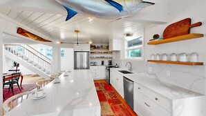 A modern kitchen with white cabinetry, a marble countertop, a stainless steel refrigerator, and a red patterned rug. - Updated Oceanfront home, large yard, private beach access, screened porch! (Isle of Palms)
