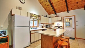 A kitchen with a refrigerator, wooden cabinets, a sink, and a wooden island with stools.