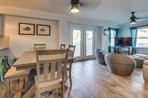 A dining area with a wooden table and chairs, a television in the living room, and wicker furniture.
