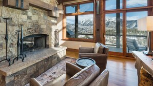 A stone fireplace with a metal screen, a leather sofa, a round coffee table, and a large window with a mountain view.