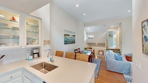 A modern kitchen with a central island, a dining area with wicker chairs, and a living room with a sofa and a painting. - Villa in Wild Dunes with golf and Lagoon views; close to pool (Isle of Palms)