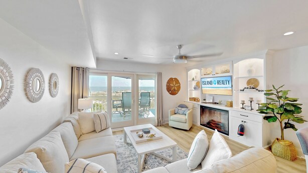 Uma sala de estar espaçosa com um sofá grande, uma mesa de centro e uma lareira. Há uma televisão na parede exibindo 'ISLAND REALTY'.