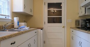 A compact kitchen with white cabinets, a sink, a microwave, and a coffee maker.