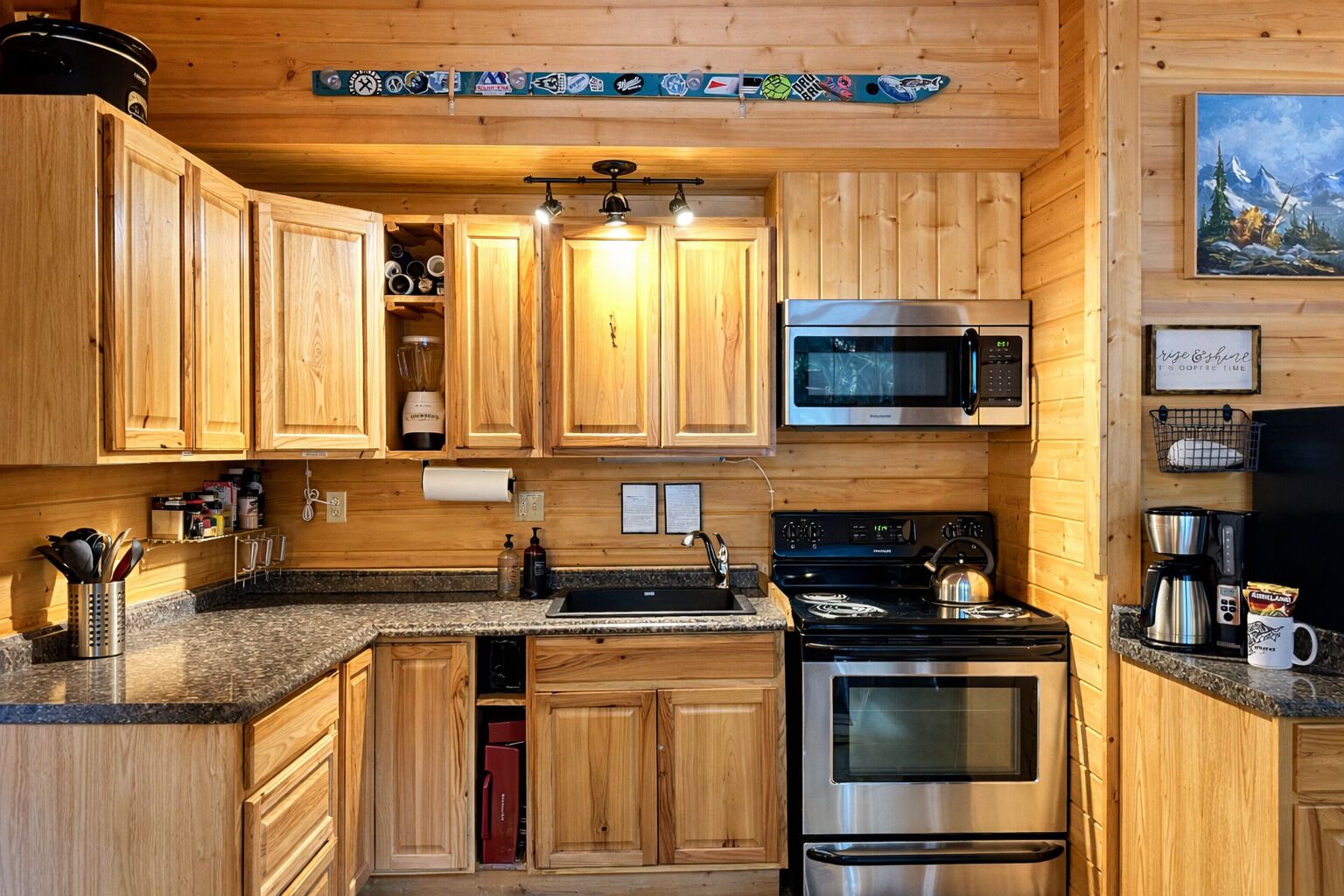 A wooden kitchen with a microwave, stove, and oven. There are wooden cabinets and a granite countertop.