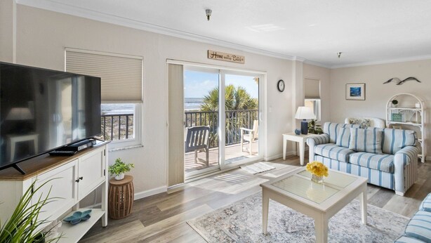Una sala de estar con televisor, sofá, mesa de centro y balcón con vista a la playa.