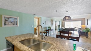A modern kitchen with granite countertops, stainless steel sink, and a dining area with a wooden table and chairs. - Beachfront Complex - 2b 2b - Beach Place #303 (Madeira Beach)