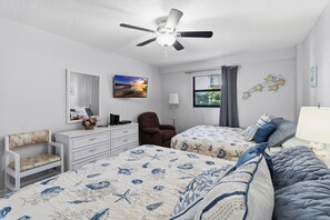 A bedroom with two beds, a ceiling fan, a dresser, a chair, a mirror, a window with curtains, and wall art. - Beachfront Complex - 2b 2b - Beach Place #203 (Madeira Beach)