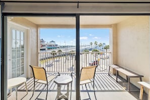 A balcony with two tables and chairs, a view of a beach, and a building in the background.