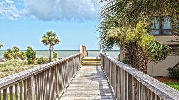 A wooden boardwalk leading to a beach with palm trees and a clear sky. - Stunning oceanfront condo located in Wild Dunes with ocean and golf views (Isle of Palms)