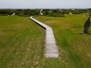A wooden boardwalk leading through a grassy field towards a beach.