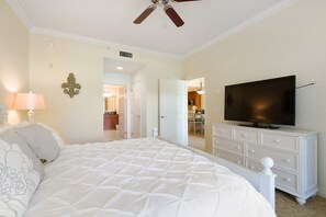 Une chambre à coucher avec un grand lit, un téléviseur posé sur une commode et un ventilateur de plafond.