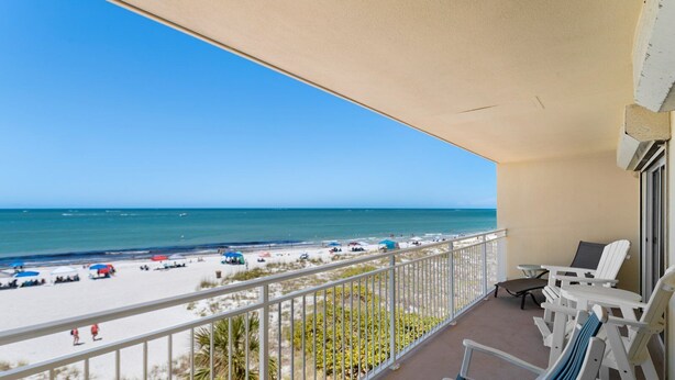 A balcony with a view of a beach and ocean. There are white chairs and a small table on the balcony. - Prime Beachfront Balcony - Madeira Norte #311 (Madeira Beach)