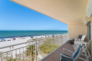 Een balkon met uitzicht op een strand en zee. Er staan witte stoelen en een tafeltje op het balkon.