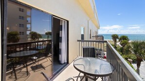 A balcony with a glass door leading to a pool area, a small table, and chairs. - Beach View 1b 1b - Balcony - King - Surf Song #345 (Madeira Beach)