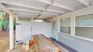 A covered patio with a wooden table and benches, a white fence, and a window with blinds. - Pet friendly with fenced yard, no stairs, walk to beach access, sleeps 6! (Isle of Palms)