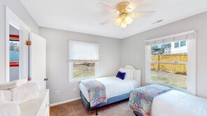 A bedroom with two beds, a ceiling fan, and a window with a view of a backyard. - Pet friendly with fenced yard, no stairs, walk to beach access, sleeps 6! (Isle of Palms)