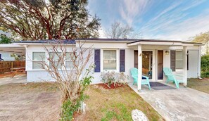 A single-story house with a porch, two windows with shutters, and a small garden area with a tree and shrubs. - Pet friendly with fenced yard, no stairs, walk to beach access, sleeps 6! (Isle of Palms)