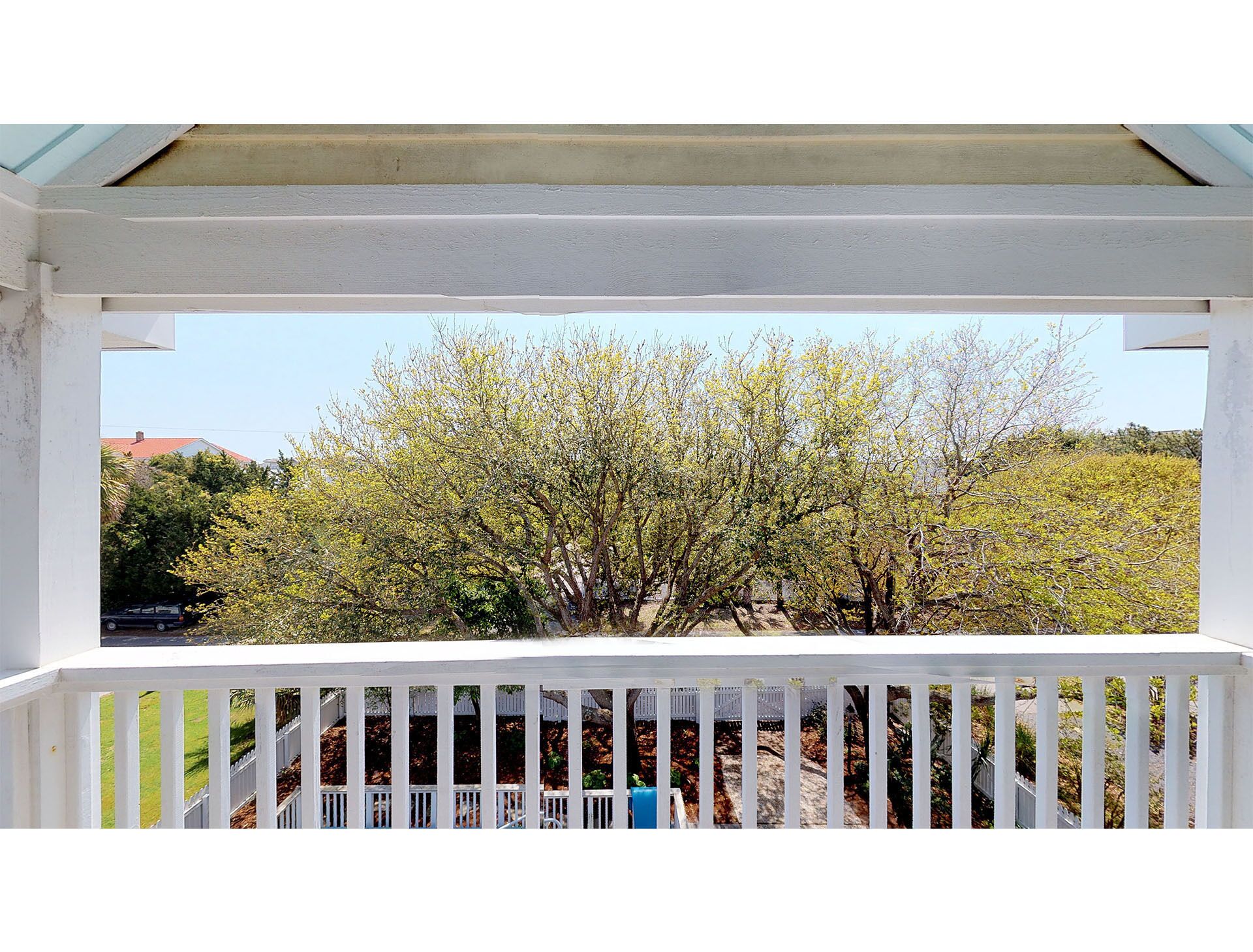 A white balcony with a view of a tree and a distant building.