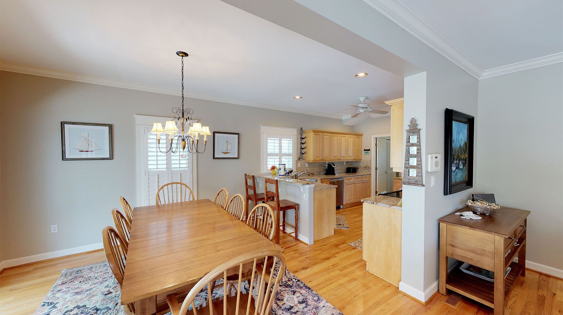 A spacious dining area with a wooden table and chairs, a chandelier, and a kitchen in the background.