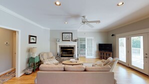A spacious living room with a fireplace, a ceiling fan, and a large window.