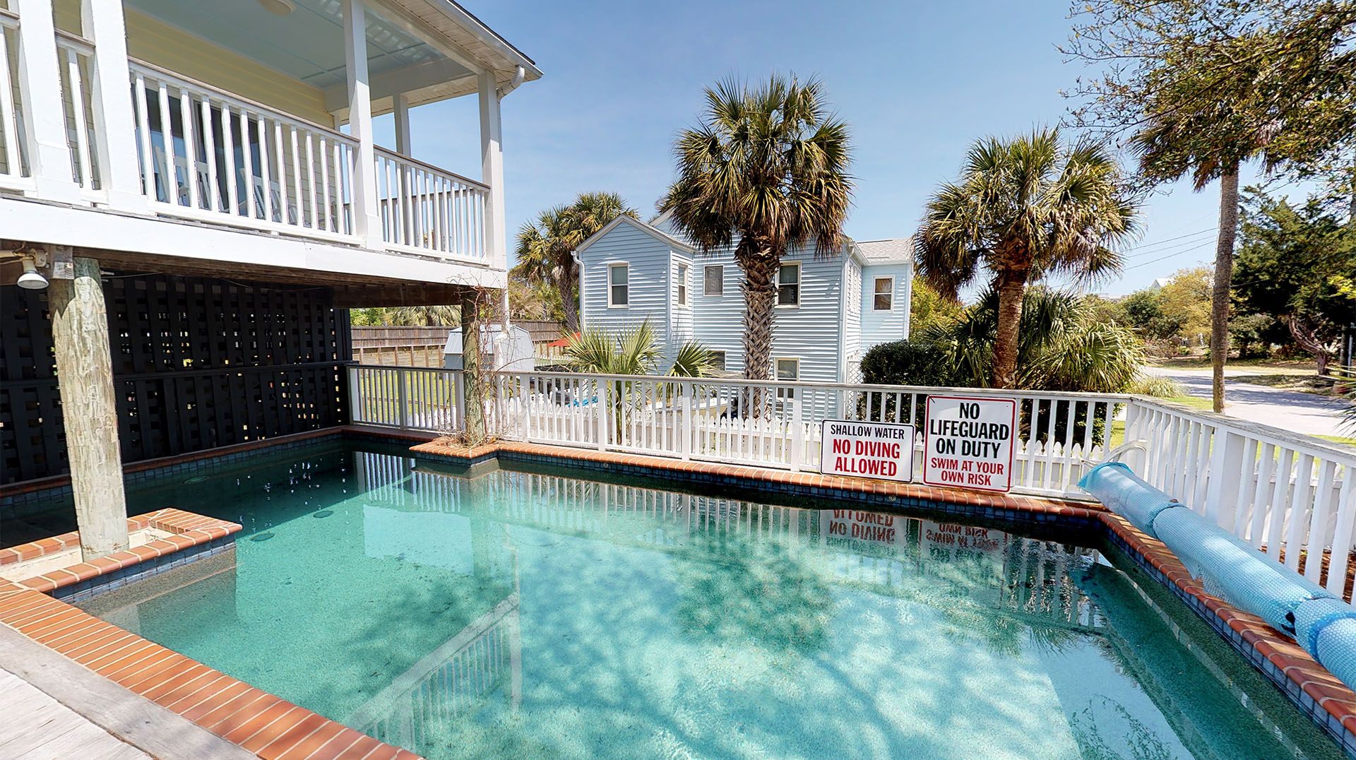 A swimming pool with a white fence, surrounded by palm trees and a house.