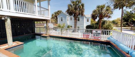 A swimming pool with a white fence, surrounded by palm trees and a house.