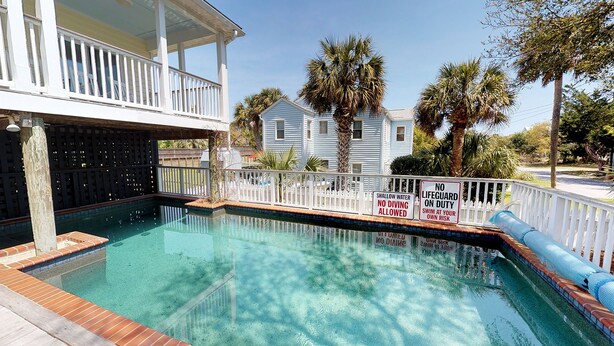 A swimming pool with a white fence, surrounded by palm trees and a house.